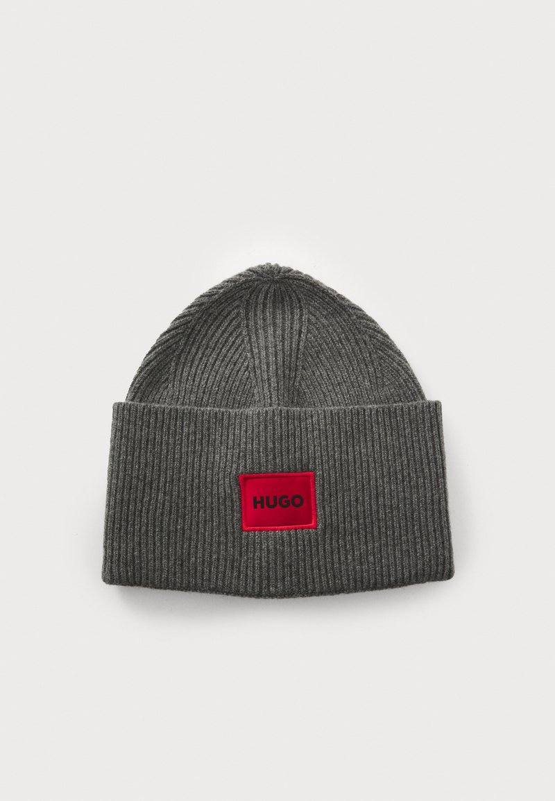 Beanie grigia a coste con risvolto, caratterizzata da un'etichetta rettangolare rossa con "HUGO" stampato in nero.