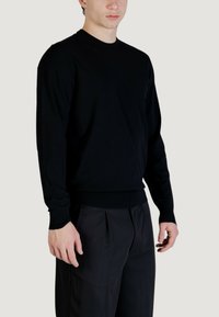 Maglione nero girocollo in tessuto morbido con maniche lunghe e polsini e orlo a coste, abbinato a pantaloni scuri.