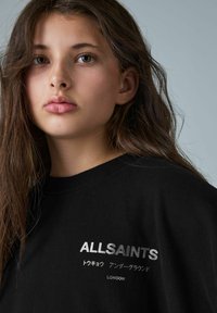 Juoda palaidinė su užrašu "ALLSAINTS" ir sidabro spalvos japonų simboliais, apvaliu kaklu ir minkšta audinio tekstūra.