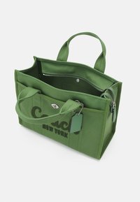 Grön tygkasse med dubbla handtag, dragkedjestängning, innerficka och präglad "Coach New York"-logotyp på framsidan.