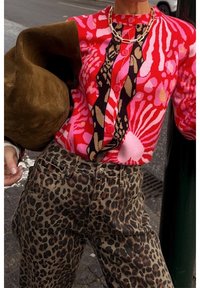 Cárdigan de punto colorido con patrones florales en rojo y rosa con acentos negros, combinado con jeans marrones con estampado de leopardo. Textura de tela suave.