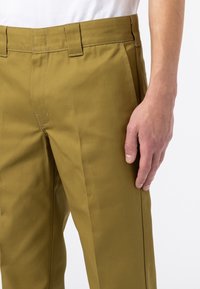 Olivgröna byxor i slitstarkt tyg med rak passform, bälteshällor och en slät textur med subtila sömdetaljer.