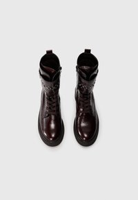 Brown leather ankle boots with a glossy finish, lace-up front, and decorative studs. Features a rounded toe and thick black sole.