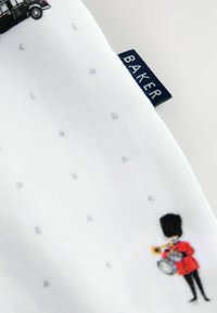 Vitt tyg med färgglada illustrationer av ikoniska Londonsymboler, inklusive en svart taxi och en bandmedlem i röd uniform. Märkets etikett synlig.