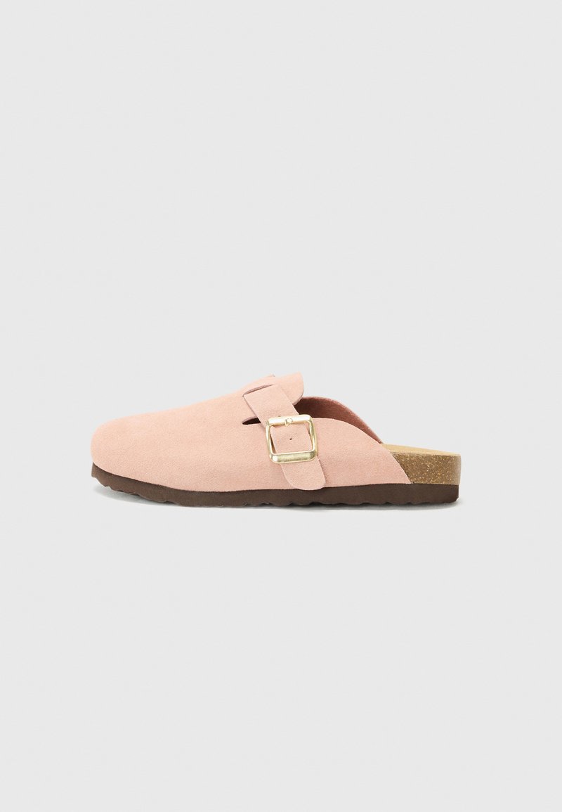 Clog de camurça rosa claro com uma única alça e fivela dourada, palmilha texturizada e sola de borracha marrom.