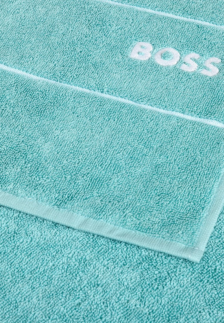 Heller blauer Frotteehandtuch mit weißem gesticktem "BOSS"-Text nahe der Kante, der Textur und gefaltetem Ecken zeigt.