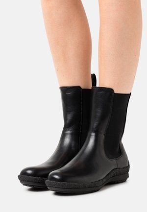 Bottines noires avec une tige en cuir lisse, des panneaux latéraux en élastique, un bout rond et une semelle en caoutchouc texturée. Elles sont dotées d'une languette à l'arrière.