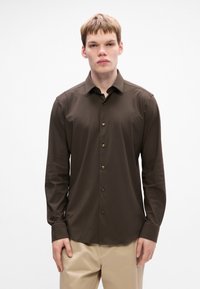 Camisa de botón de manga larga marrón con una textura suave, que presenta un collar puntiagudo, botones dorados y puños; combinada con pantalones de color claro.