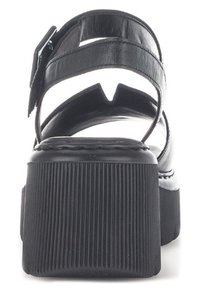 Sandales en cuir noir avec une semelle plateforme, présentant une texture côtelée et une bride de cheville réglable avec une boucle en métal.