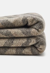 Vævet tæppe i beige og grå med ternet mønster. Blød tekstur, foldet, der fremviser tykkelse og stofdetaljer.
