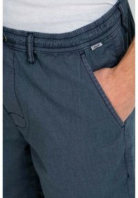Pantalones cortos de color azul oscuro hechos de tejido texturizado, con cinturilla elástica, bolsillos laterales y una pequeña etiqueta de marca cerca de la cintura.