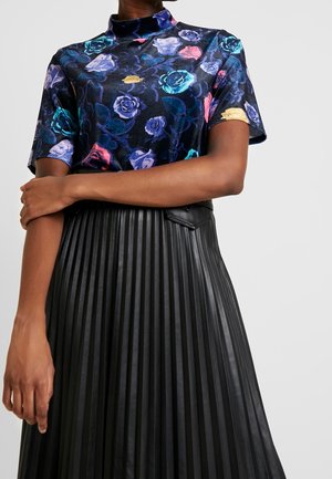 Nainen pukeutuneena mustaan, laskostettuun nahkahameeseen ja lyhythihaiseen samettiseen kukkakuosiseen toppiin, jossa on sinisiä, purppuranvärisiä, keltaisia ja vaaleanpunaisia ruusuja.