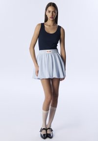 Canotta blu navy, gonna a righe azzurre chiare con cintura elastica e logo, abbinata a calze fin sopra il ginocchio beige e ballerine nere.