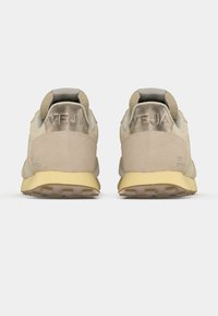 Μπεζ σουέντ αθλητικά παπούτσια με υφή, που διαθέτουν ασημένιο λογότυπο στη φτέρνα και κίτρινη ελαστική σόλα με σχέδια για πρόσφυση.