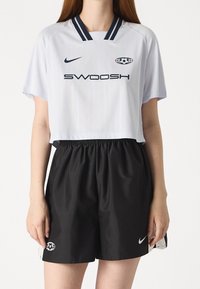 White short-sleeve cropped jersey with navy vertical stripes and "SWOOSH" text, paired with black elastic waistband shorts featuring Nike logo.
