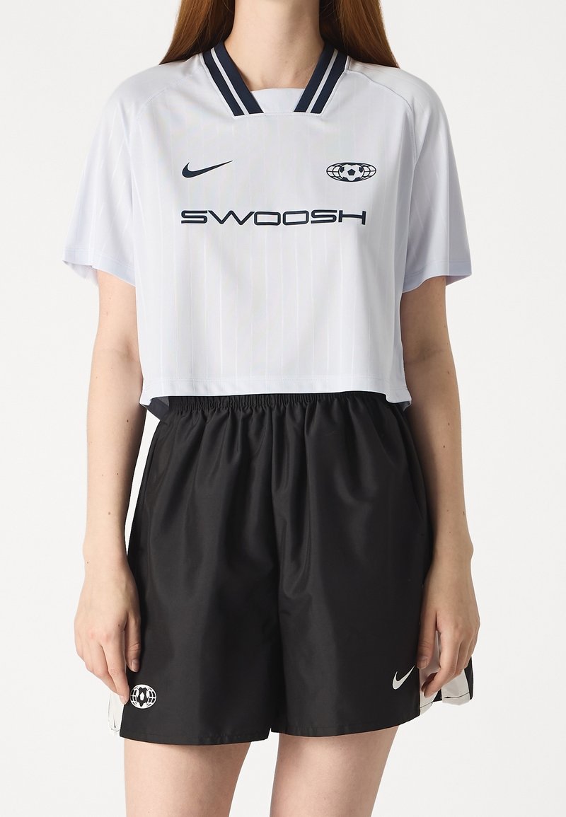 White short-sleeve cropped jersey with navy vertical stripes and "SWOOSH" text, paired with black elastic waistband shorts featuring Nike logo.