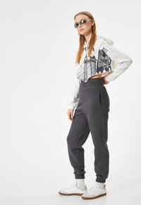 Afskåret hvid hoodie med grafisk design, parret med mørkegrå sweatpants med elastisk talje og manchetter, båret med hvide sneakers.