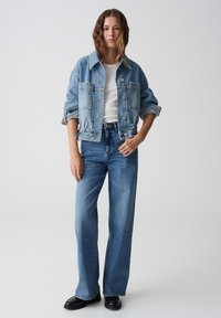Lichtblauwe denimjacket met knoopsluiting, oversized pasvorm en opgerolde mouwen, gecombineerd met hoge taille, wijde lichtblauwe jeans.