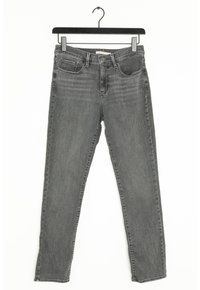 Jean slim gris avec poches avant et passants de ceinture suspendu sur un cintre noir contre un fond blanc.