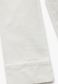 Pantalones de algodón blancos con un diseño de pierna recta y dobladillo enrollado. Detalle de costura notable a lo largo de las costuras y una textura suave.
