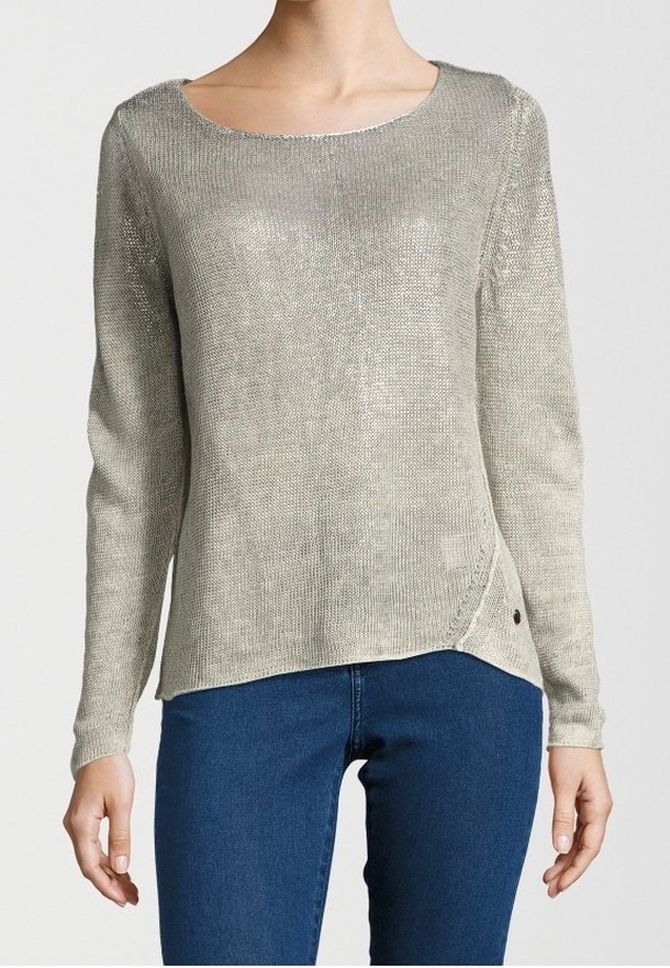 Femme portant un pull en tricot gris clair à manches longues avec un large col rond et un jean bleu foncé.