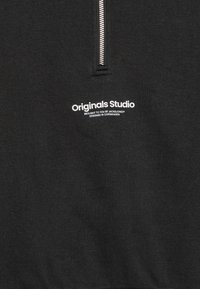 Svart half-zip sweatshirt med mykt stoff, en teksturert følelse, og hvit trykt tekst som sier "Originals Studio" foran.