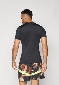 Kortærmet sort træningsshirt med en glat tekstur, sammen med multikolorede mønstrede shorts med en neongrøn detalje.