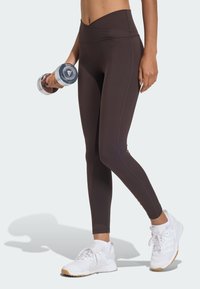 Leggings marroni a vita alta realizzati in tessuto elasticizzato, caratterizzati da una superficie liscia e dettagli di cucitura discreti, abbinati a scarpe da ginnastica bianche.