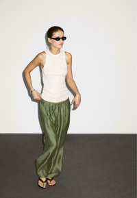 Lichtgrijze mouwloze top gecombineerd met losse, olijfgroene broek en zwarte zonnebril. De broek heeft een gatherede taille en een soepele textuur.