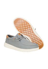 Zapatillas de lona grises con un acento de cuero marrón, suela de goma blanca con un patrón en cuadrícula y diseño de puntera redondeada con cordones.