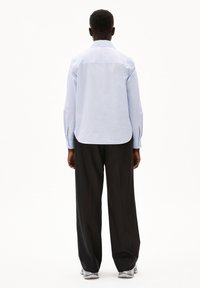 Lichtblauw longsleeve shirt met een kraag, rechte zoom en zijsplitten, gecombineerd met losse zwarte broek. Soepele textuur.