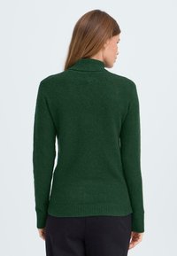 Groene gebreide coltrui met lange mouwen, geribbelde manchetten en onderrand, met een textuur van zacht, pluizig garen.