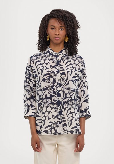 Blusa de color navy con patrones florales blancos, cierre de botones y mangas tres cuartos. Fabricada con un tejido ligero y de corte relajado.