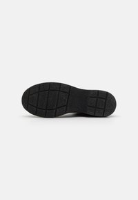 Suela de zapato de goma negra con patrón de agarre texturizado, con una punta redondeada y un tacón plano, diseñada para estabilidad y tracción.