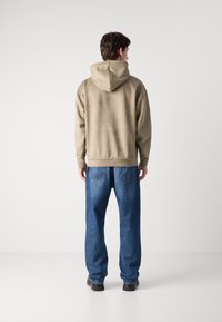 Sweatshirt bege com capuz e um corte descontraído, combinado com jeans de ganga azuis largos. Apresenta um bolso canguru e punhos canelados.