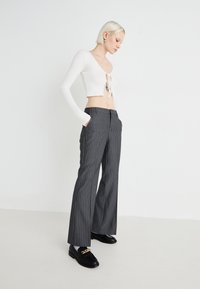 White ribbed crop top with tie detail, paired with gray striped wide-leg trousers. Model wears black loafers with gold accents, standing on plain background.