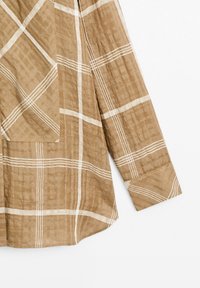 Bruine geruite shirt met een losse pasvorm, gekenmerkt door witte gridlijnen en een textuurstof. Inclusief een opgestikte zak aan de linkervoorzijde.