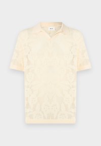 Κρεμ πλεκτό πόλο μπλουζάκι με κοντά μανίκια, διακοσμημένο με σχέδιο λουλουδιών από δίχτυ και με μυτερό γιακά, παρουσιάζεται σε απλό φόντο.