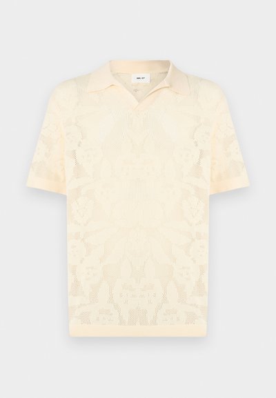 Polo tricoté à manches courtes couleur crème avec motif floral en maille et col pointu, présenté sur un fond uni.