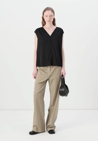 Top nero a maniche corte con scollatura a V, abbinato a pantaloni beige a righe a gamba larga e una piccola borsa nera. Tessuto morbido, vestibilità rilassata.