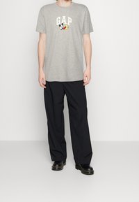 Grå bomuld t-shirt med "GAP" logo og trykt tegneseriefigur, parret med sorte løstsiddende bukser og sorte støvler.