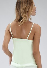Lichtgroene satijnen camisole met dunne verstelbare bandjes, een gladde textuur en een rechte halslijn, met een vloeiende silhoutte.