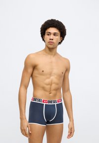 Tumši zili bokseršorti ar kontrastējošu baltu gumiju, uz kuras ir sarkans "DIESEL" uzraksts. Mīksts materiāls, pieguļošs dizains, vidēja garuma griezums.