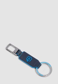 Metal and navy blue leather keyring with blue logo and silver clip on a gray background.