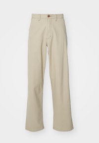 Pantalon en coton beige à jambe droite, avec une fermeture à bouton visible et des détails de couture subtils. Texture lisse, sans motifs.