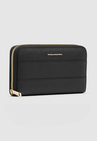 Cartera de cuero negra con superficie texturizada, cierre de cremallera y logo en tono dorado. Presenta detalles de paneles horizontales y acentos dorados en la cremallera.