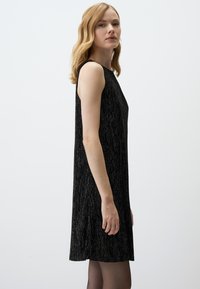 Schwarzes ärmelloses Kleid mit geradem Schnitt, aus einem strukturierten Stoff mit silbernen Fäden, knielang, mit einem schlichten Ausschnitt.