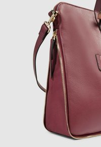 Borsa a mano in pelle color granato con una forma strutturata, caratterizzata da una cerniera dorata e una tracolla staccabile. Tessuto liscio con una finitura raffinata.