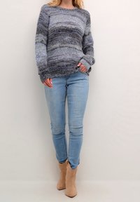 Stickad blå och grå tröja med avslappnad passform, rund halsringning och långa ärmar; kombinerad med ljusblå smala jeans och beige ankelstövlar.