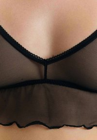 Zwarte mesh bralette met een golvende onderrand, delicate kantafwerking en een V-halsontwerp met een naad in het midden. Zachte, doorschijnende textuur.